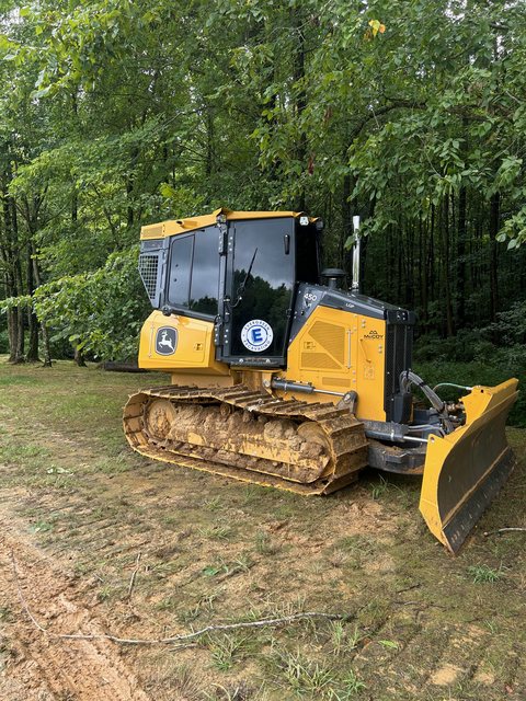 Yellow crawler dozer with dark tinted cab glass at the edge of a treeline