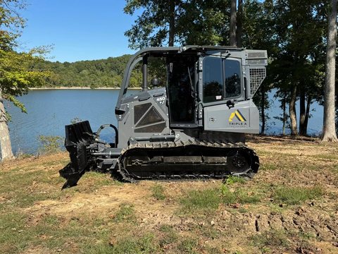 Tracked forestry mulcher with tinted cab glass beside a lake